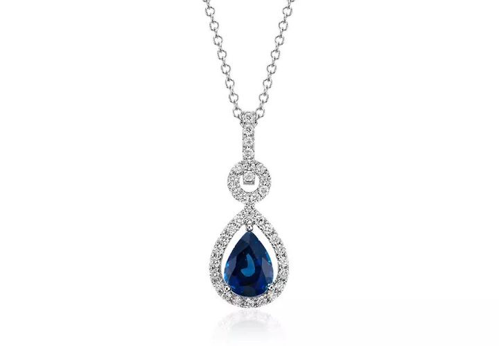 A pear-shaped dangling sapphire gemstone is suspended in a floating halo of pavé-set round diamonds in this diamond and white gold pendant